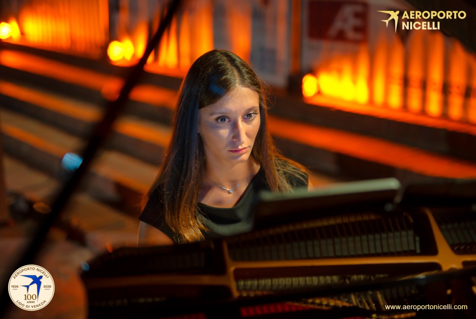 Una musicista suona il pianoforte in un ambiente illuminato con tonalità calde, mostrando un'espressione concentrata.